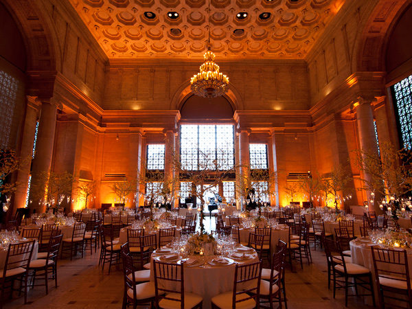 Round dinner tables with elaborate table settings inside a moodily lit ballroom.